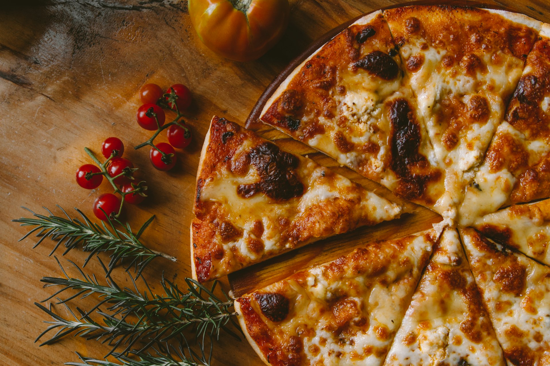 Frisch gebackene Steinofen-Pizza auf rustikalem Holz mit Tomaten und Rosmarin